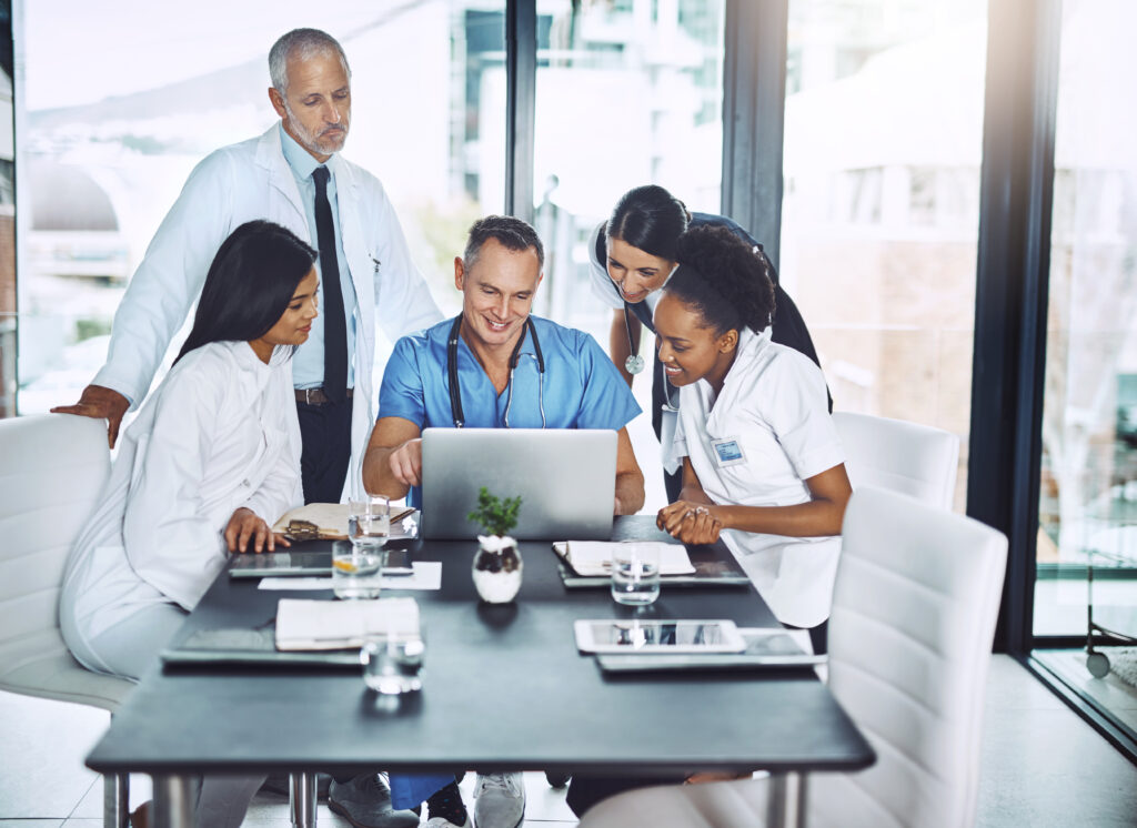 Group of medical doctors and nurses reviewing medical coding data on a laptop in a conference room.