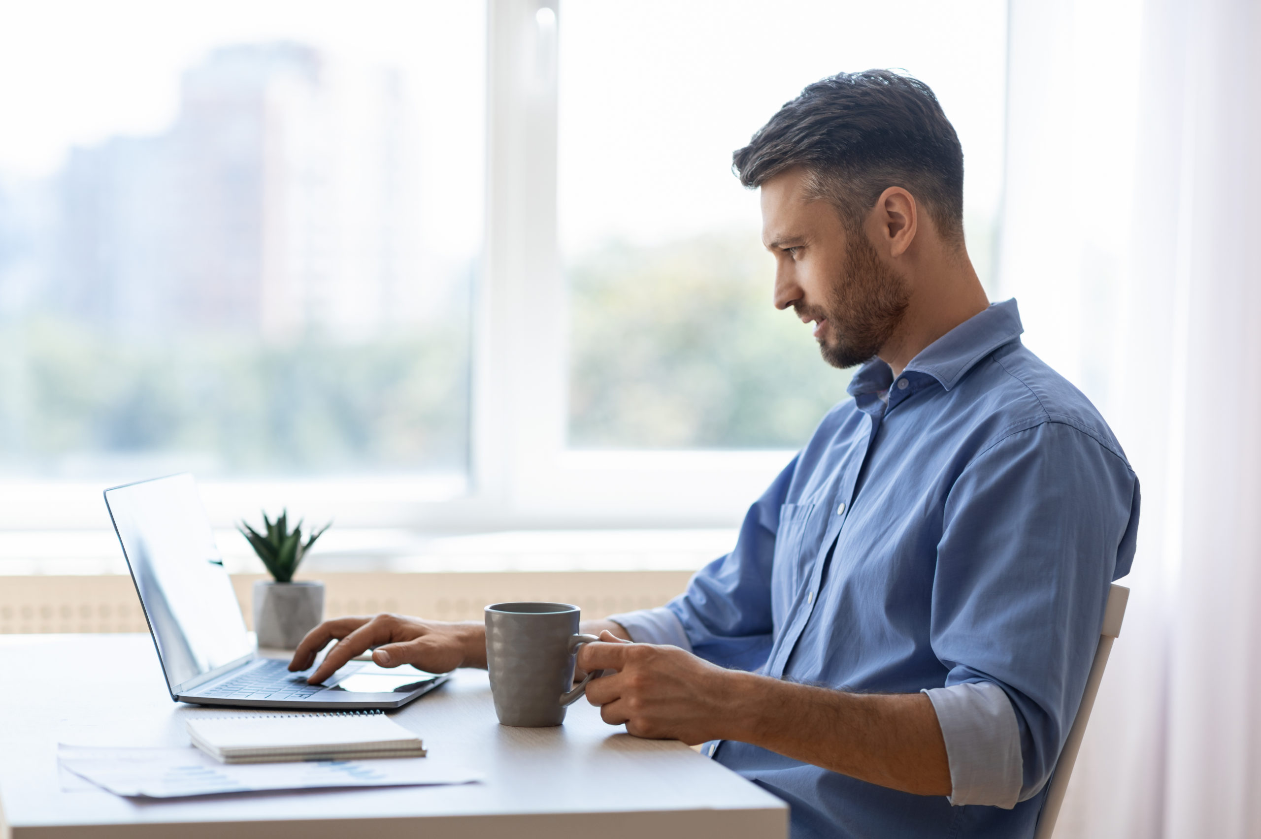Male freelance healthcare worker working remotely on his laptop with a cup of coffee