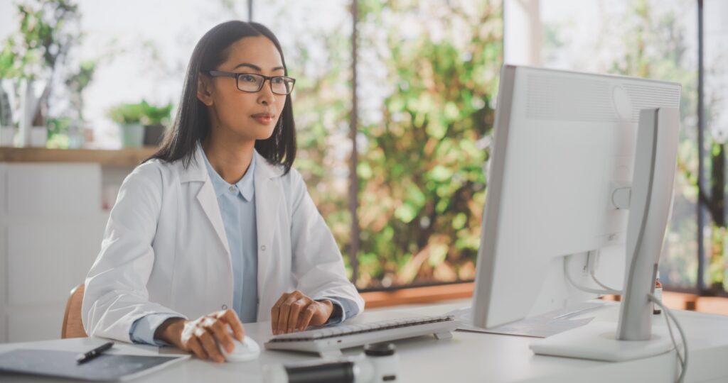 Female doctor focused on clinical documentation improvement (CDI) while working at a desktop computer in a hospital.