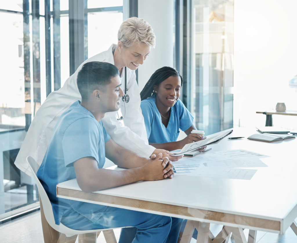 Doctor and two nurses reviewing medical documentation in a hospital conference room as part of a Super User program for EHR support.